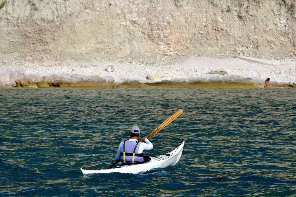 Hombre practicando kayak en aguas tranquilas junto a una playa rocosa en el Dodecaneso, Grecia