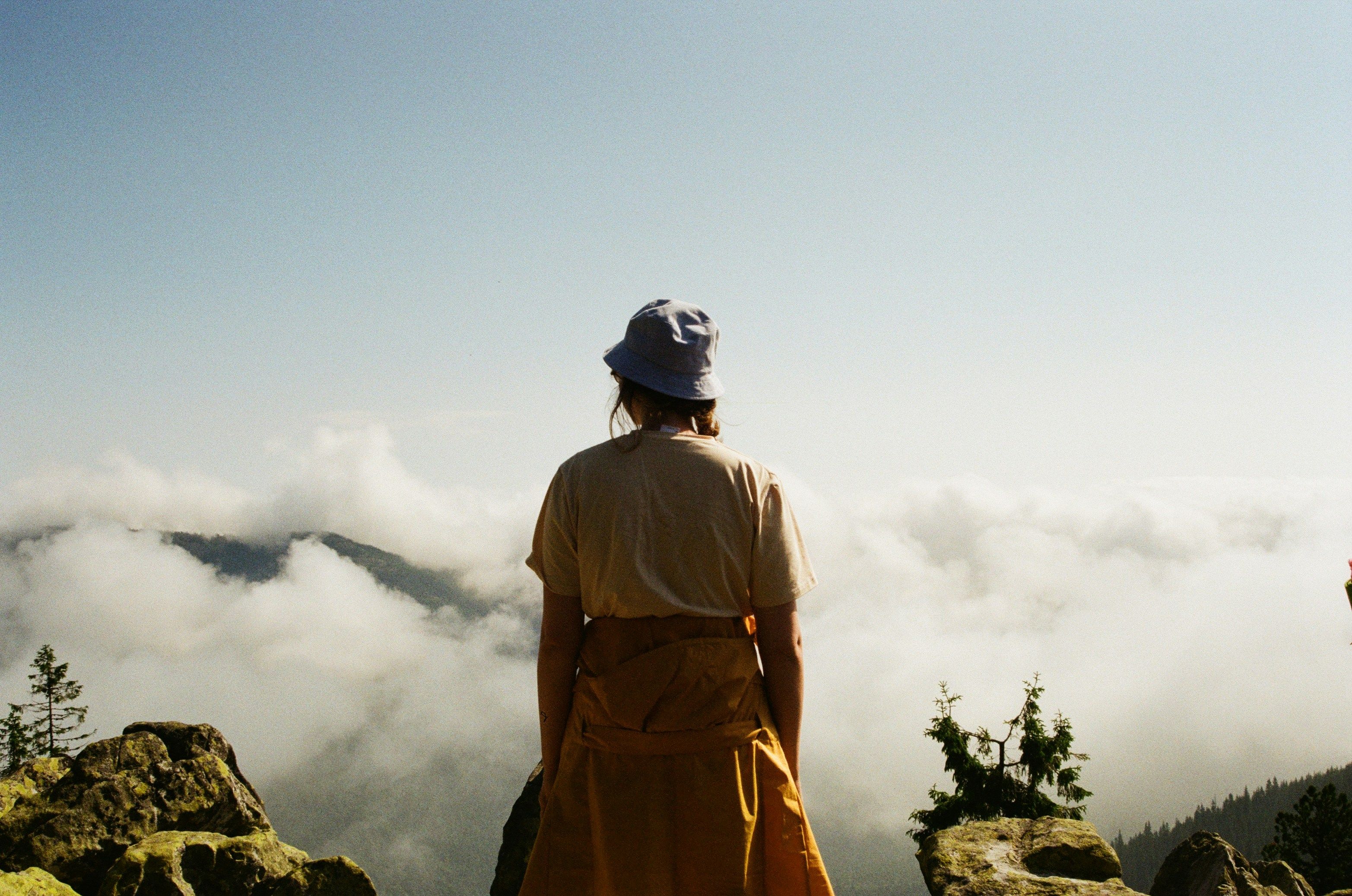 Eine Person steht mit dem Rücken zur Kamera. Sie befindet sich über den Wolken auf einem Berg und schaut auf die Wolkenlandschaft hinaus.