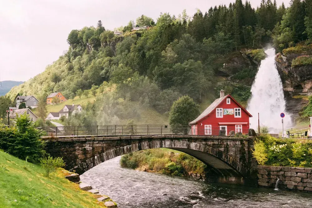 A red timber house near a bridge with a waterfall in the backdrop
