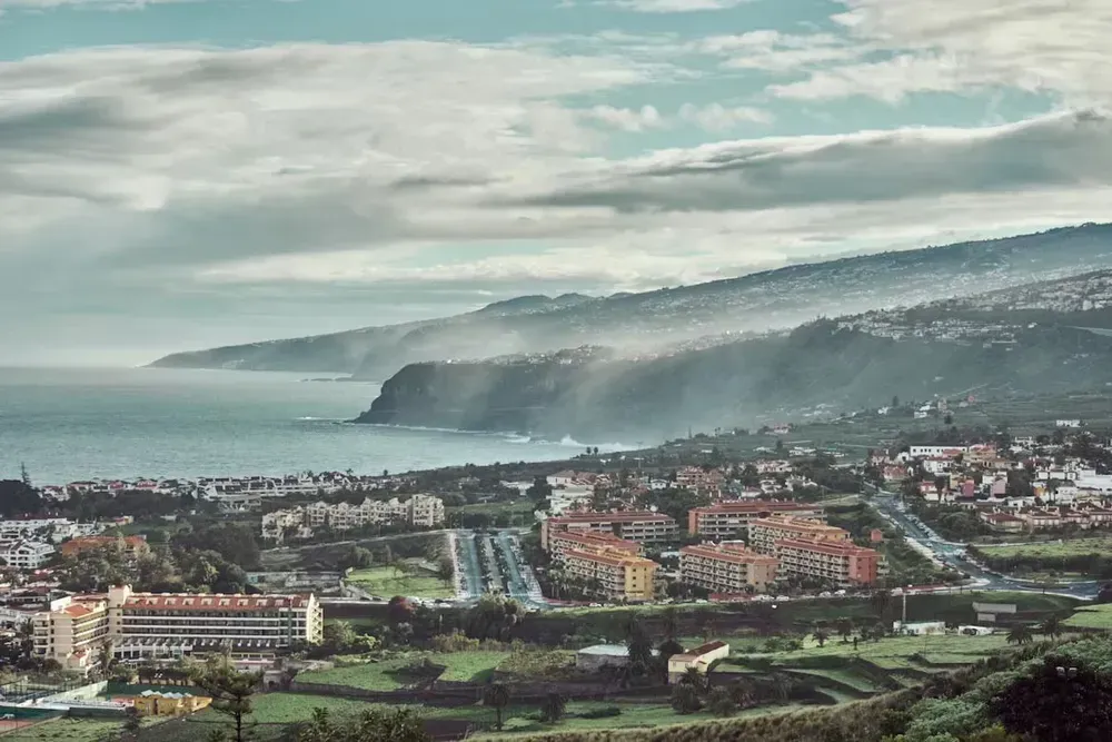 An ariel view of some hotel complexes and a sloping misty coastline in Tenerife