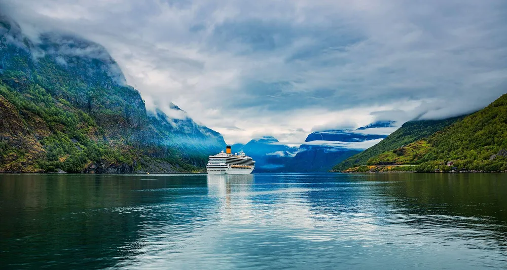 Veerboot op een turquoise fjord omgeven door groene bossen.