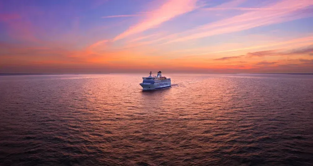Unter dem pinken Himmel des Sonnenuntergangs gleitet eine Fähre von Brittany Ferries über das ruhige Meer.