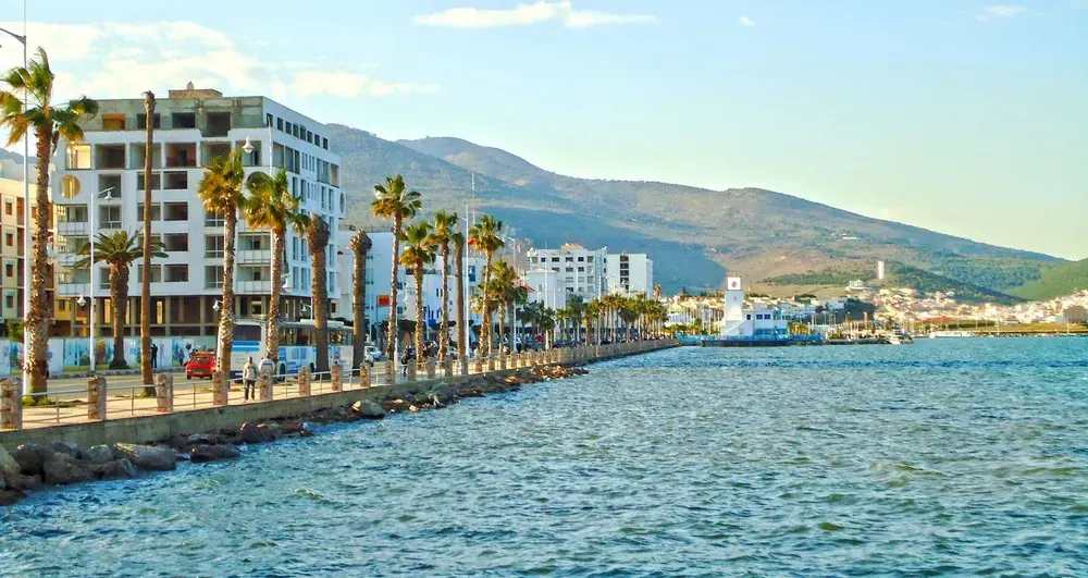 Die Uferpromenade Corniche in Nador, direkt am Meer, ist von Palmen gesäumt. Im Hintergrund sieht man einige Gebäude sowie den Berg Gourougou.