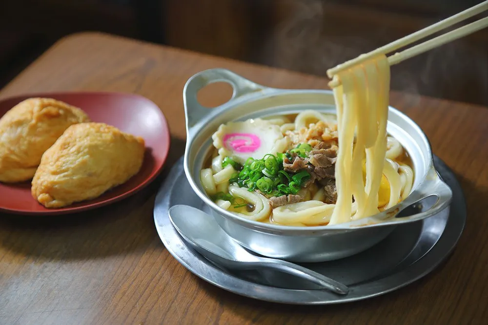 Piatto tradizionale giapponese a base di noodles in una ciotola d'argento e un piatto rosso con panini rossi.