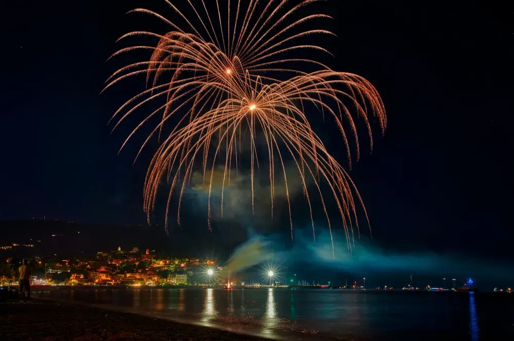 Orangenes Feuerwerk explodiert am Nachthimmel über dem Meer.