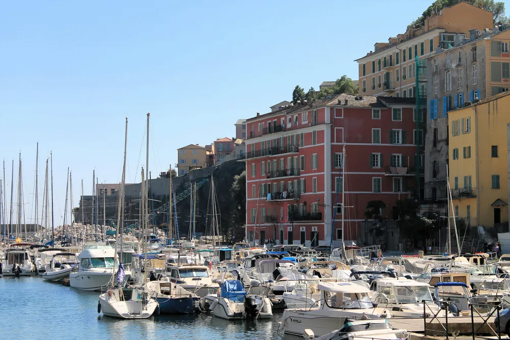 Am Hafen von Bastia liegen zahlreiche Fischerboote auf dem ruhigen blauen Wasser im Sonnenschein.