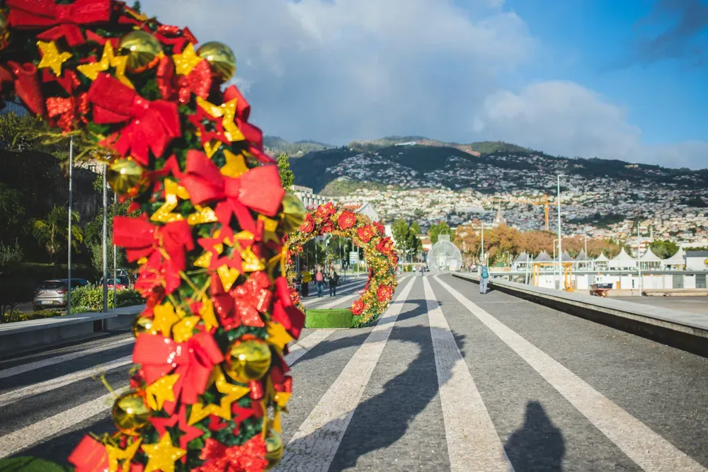 Auf Madeira stehen große Weihnachtskränze als Dekoration auf der Promenade. Im Hintergrund sieht man die Stadt.