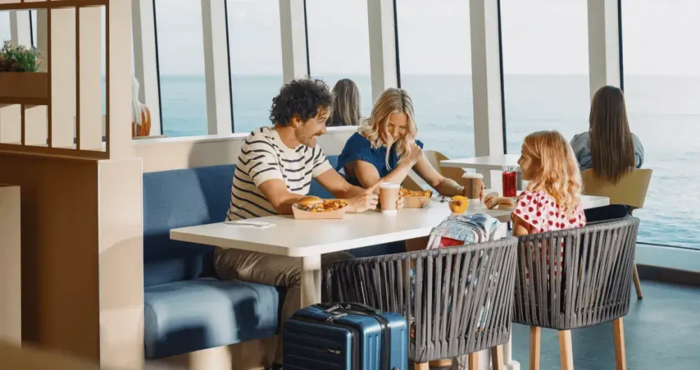 Ein Mann, eine Frau und ein Kind sitzen fröhlich an einem Tisch auf der Fähre und genießen die Überfahrt.