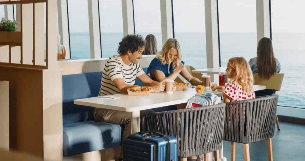 Een man, een vrouw en een kind zitten vrolijk aan een tafeltje op de veerboot en genieten van de overtocht.