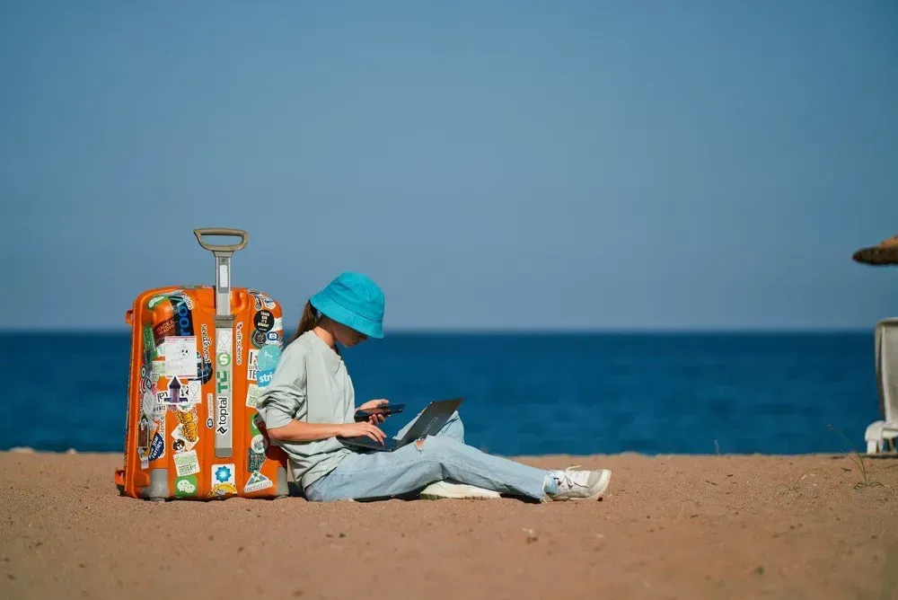 Person working with a laptop next to a suitcase on a beach in the Canary Islands.