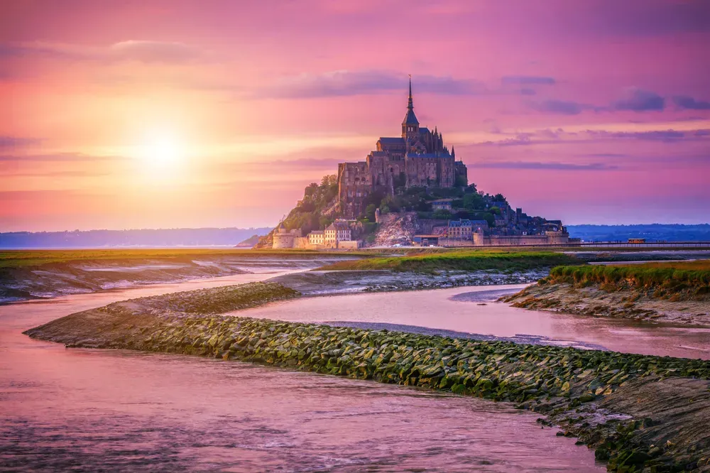 Der beeindruckende Mont Saint-Michel thront im Sonnenuntergang bei Ebbe auf der Gezeiteninsel.