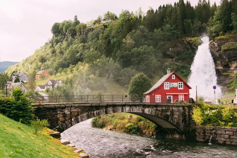 A red timber house near a bridge with a waterfall in the backdrop