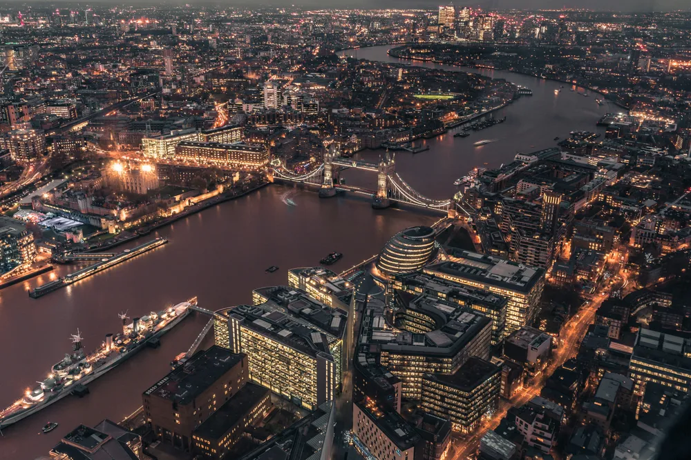 Eine Aufnahme aus der Vogelperspektive zeigt London mit dem Tower of London und der Tower Bridge bei Nacht.