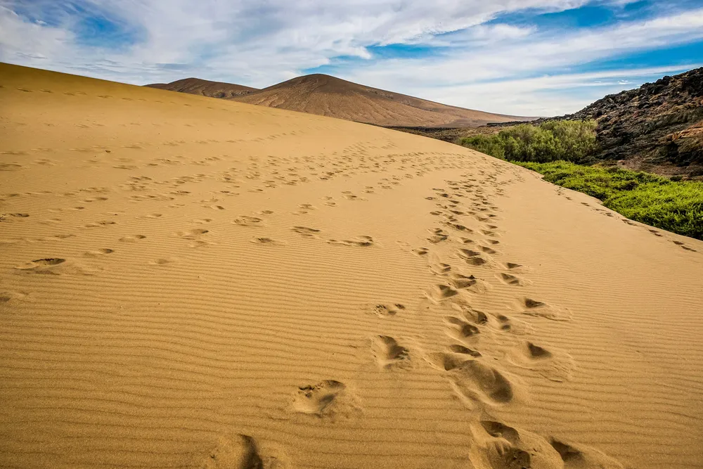 Eine große Sanddüne ist von Fußabdrücken bedeckt.