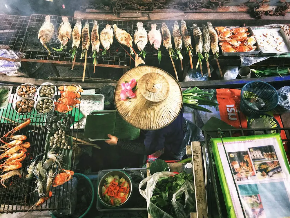 A street food vendor in a straw hat grilling white fish