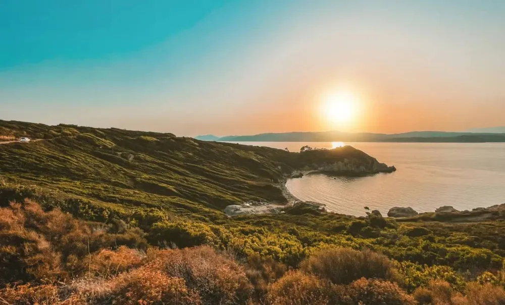 Paisaje costero con colinas verdes y una pequeña bahía al atardecer en Grecia