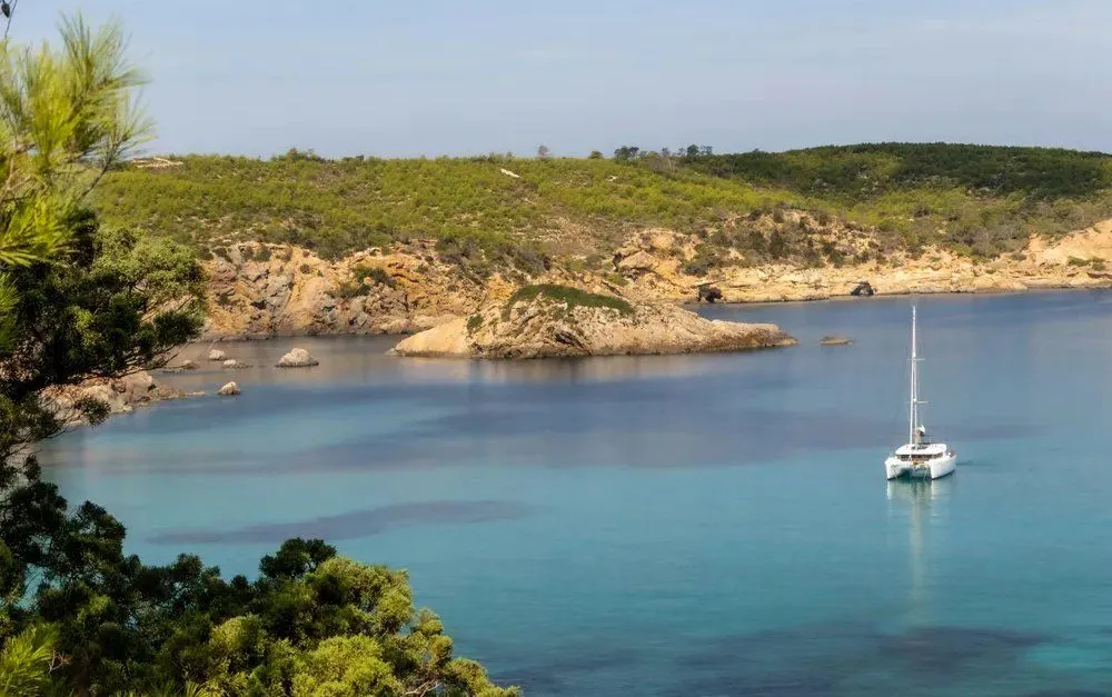 Cala tranquila con un velero sobre el mar turquesa en Ibiza durante el otoño