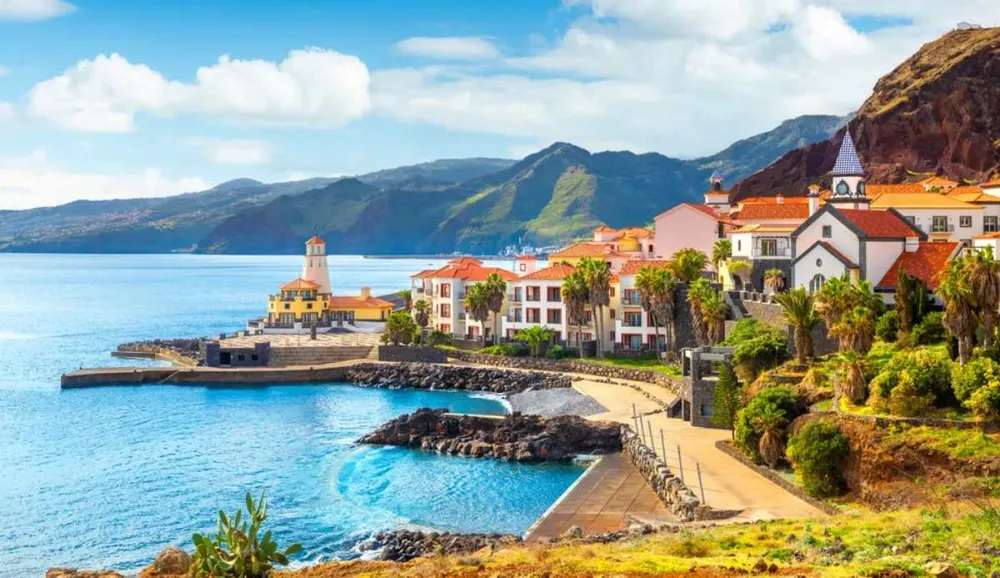 Vistas de la costa de Madeira con casas tradicionales, montañas verdes y mar azul.