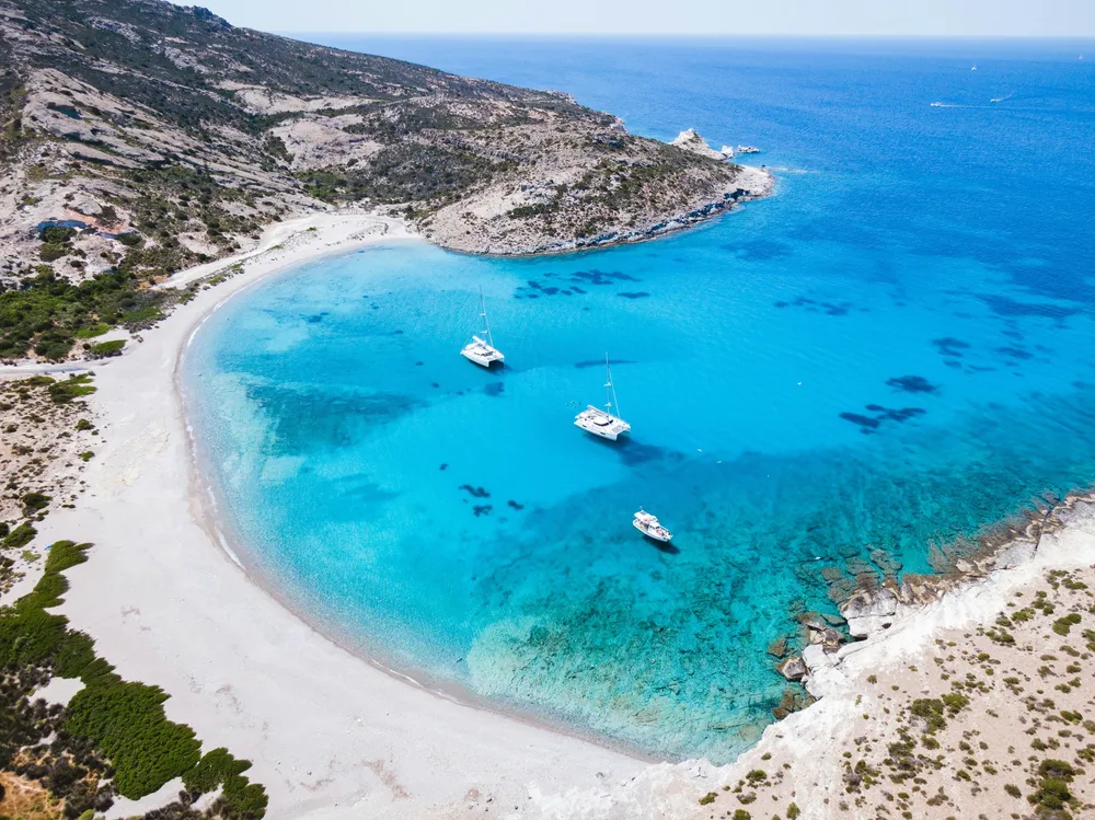 boats off the coast of a sandy bay in Milos