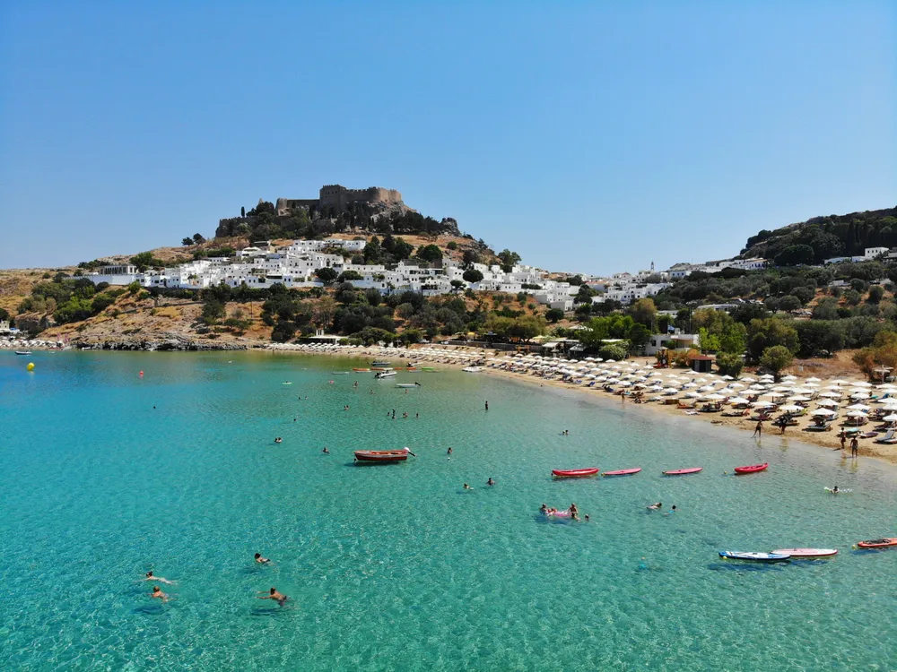 people swimming on a beach next to the mountains in Lindos