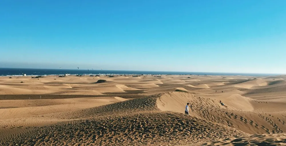 Vista panorámica de las dunas de Maspalomas en Gran Canaria, con el mar al fondo y un cielo despejado bajo la luz del invierno.