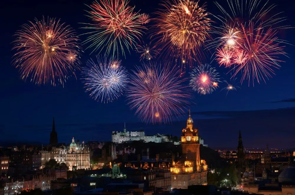 Ein strahlendes Feuerwerk an Silvester über der Skyline von Edinburgh, mit dem Schloss im Hintergrund.