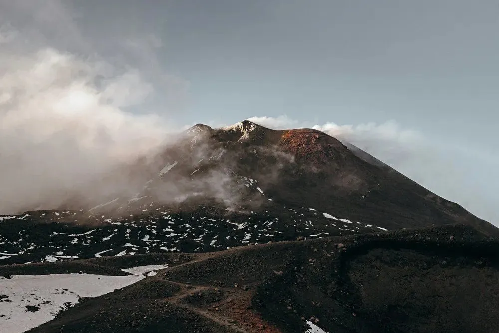 Ladera del Etna con suelo oscuro, niebla baja y manchas de nieve