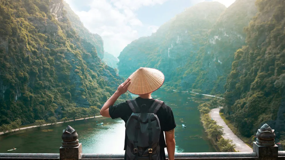 un viaggiatore con indosso un nón lá che ammira le montagne rigogliose del Vietnam