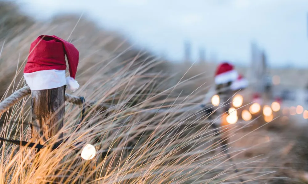 Gorros de Navidad colocados sobre postes de madera en un sendero costero iluminado