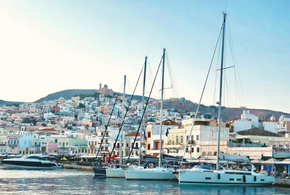 Vista del puerto de Ermoupoli en Syros con veleros y casas en tonos pastel sobre la colina