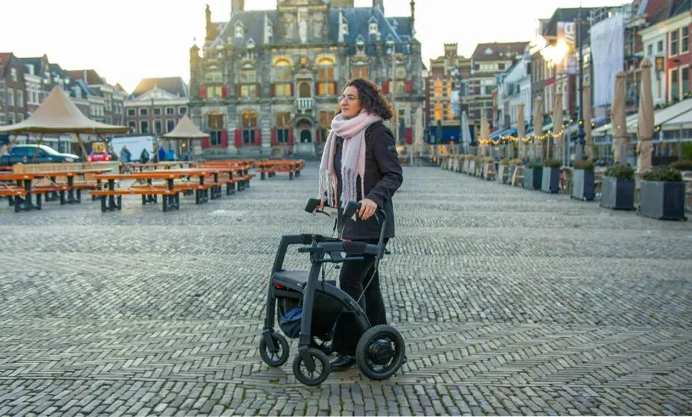 Persona caminando con un andador por una plaza peatonal, en un entorno urbano accesible con suelo pavimentado.