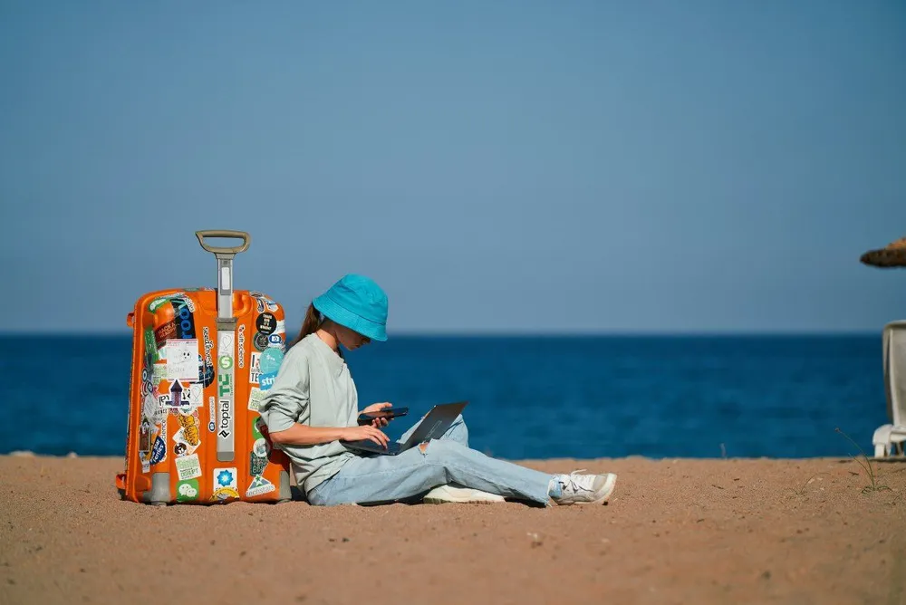 Persona trabajando con un ordenador portátil junto a una maleta en la playa de las Islas Canarias.
