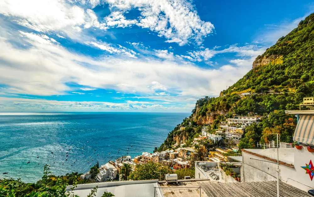 Positano con il sole, scogliere a picco sul mare e acqua turchese.