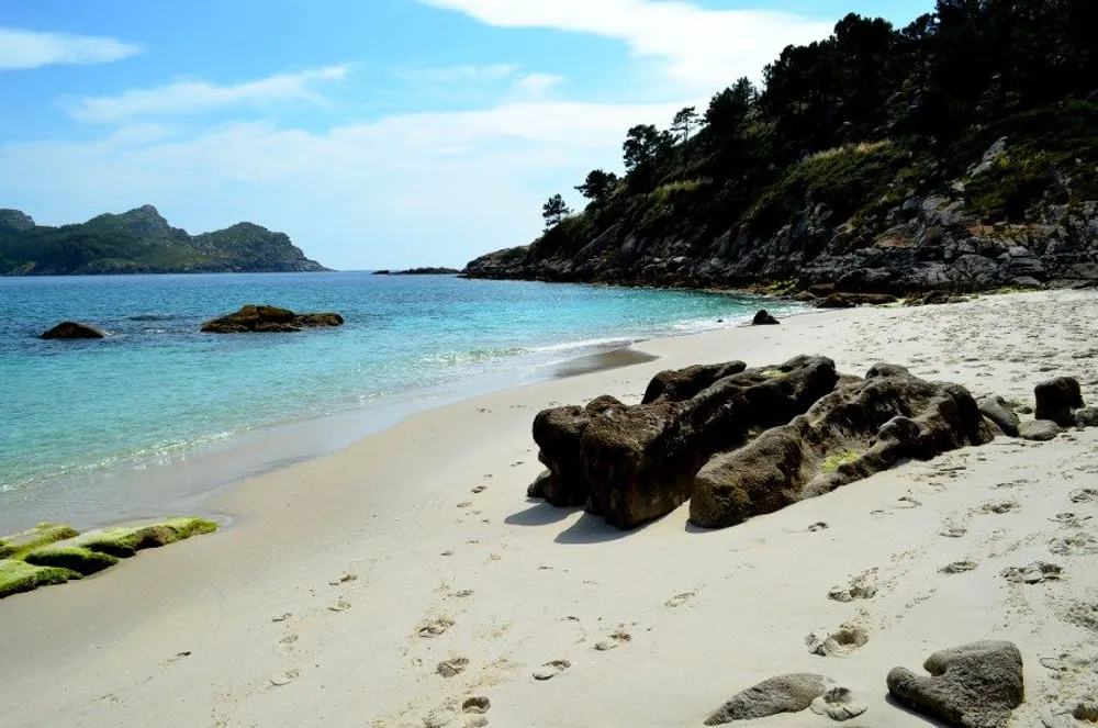 Playa virgen con aguas turquesas y rocas en la arena blanca de las Islas Cíes, rodeada de vegetación y acantilados, ideal para relajarse en plena naturaleza.