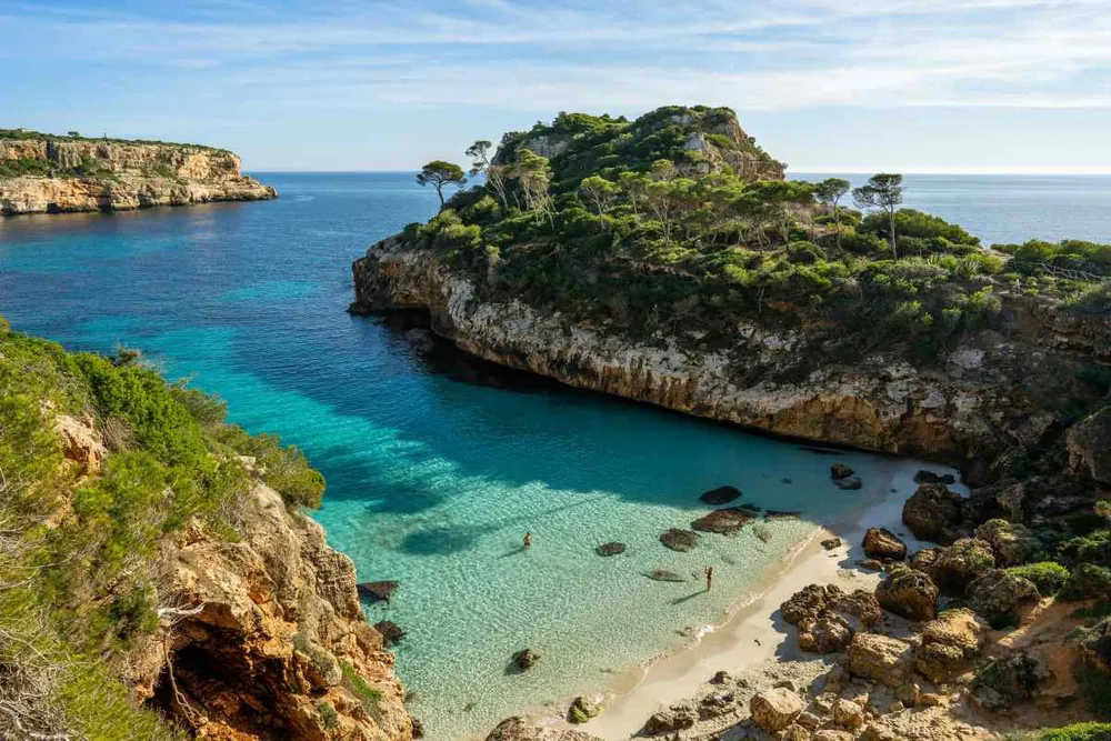 Cala de aguas turquesas rodeada de acantilados y vegetación en la costa de Mallorca con bañistas en el agua