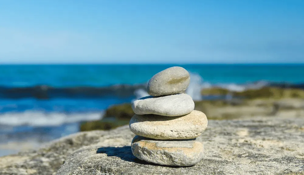 Piedras apiladas sobre una roca junto al mar, simbolizando equilibrio y tranquilidad.