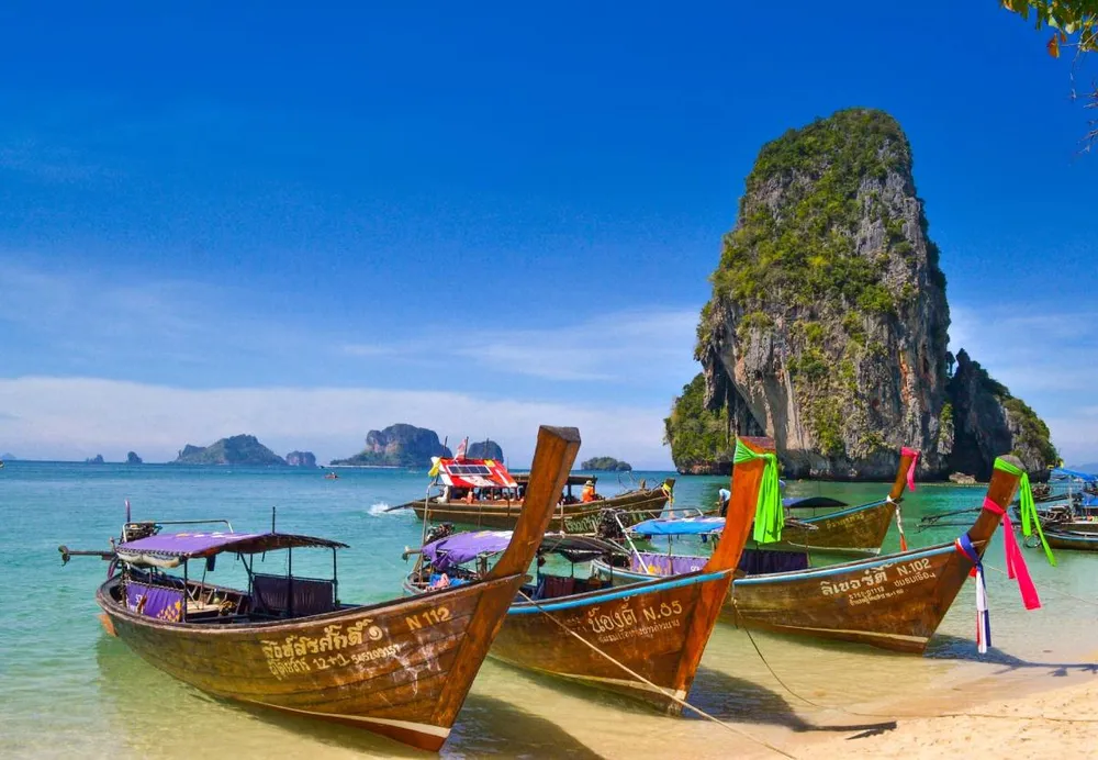 Barcas tradicionales tailandesas de madera en la playa de Railay, Krabi, con agua turquesa y formaciones rocosas de fondo.