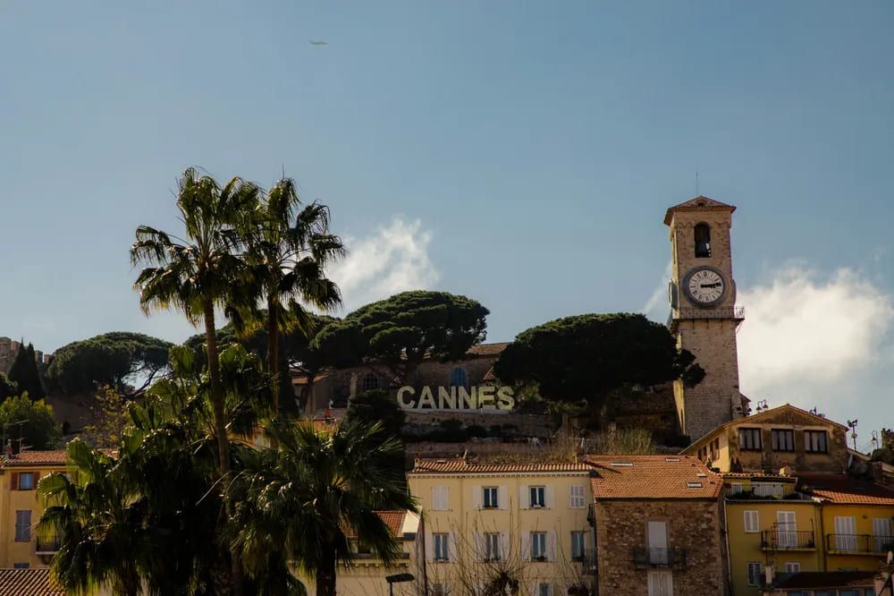 El reloj de la torre del barrio de Le Suquet y las letras 'CANNES' entre árboles y palmeras, símbolo del casco antiguo de la ciudad.