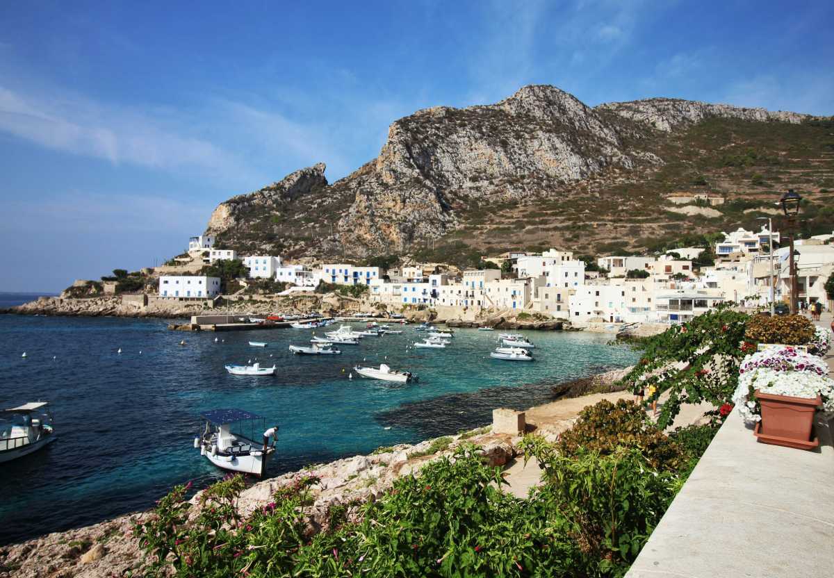 Puerto de Levanzo con casas blancas y barcas flotando, rodeado de montañas en las islas Égadas, Sicilia