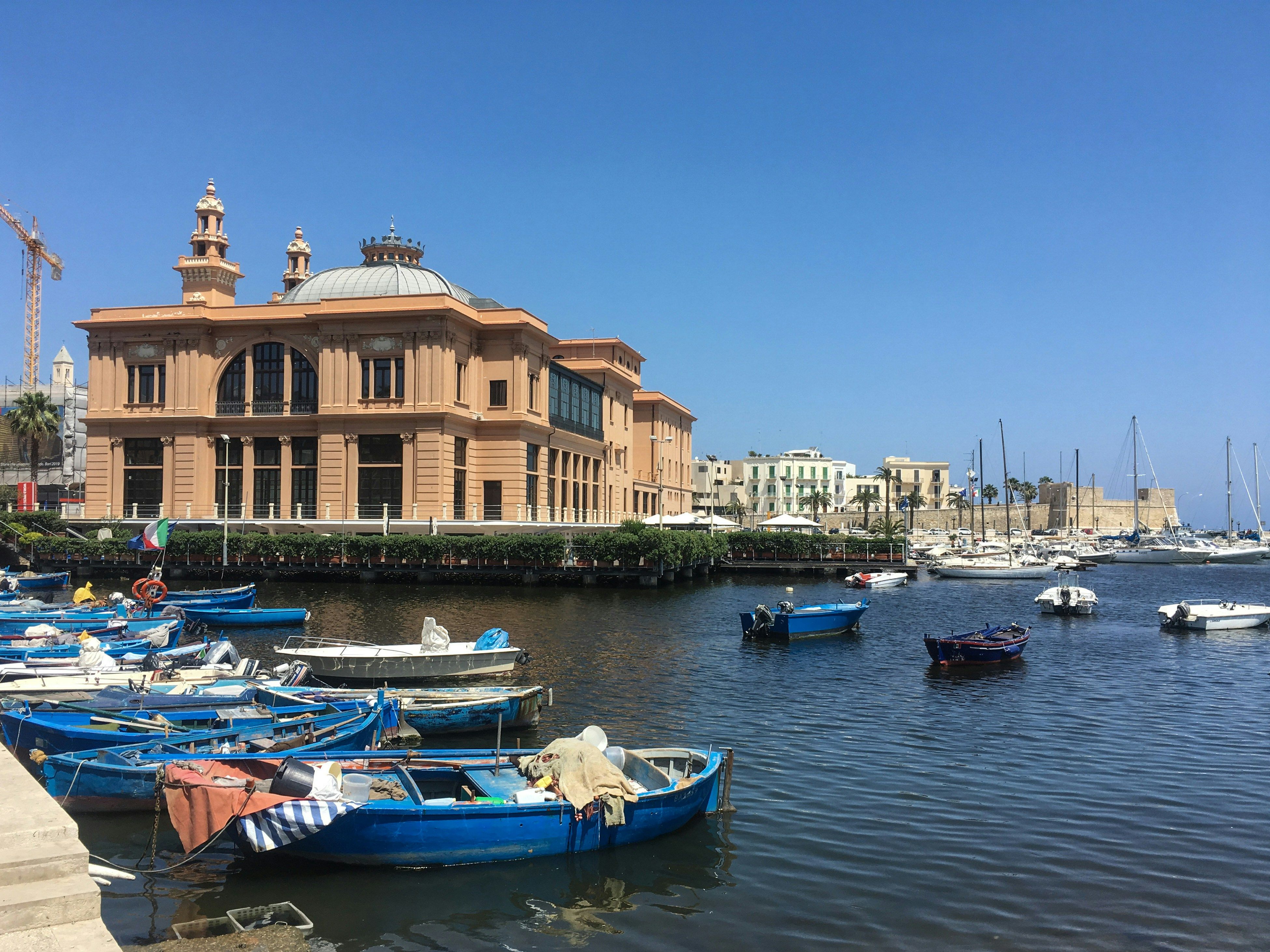 boats lined up in the water by a building in Bari