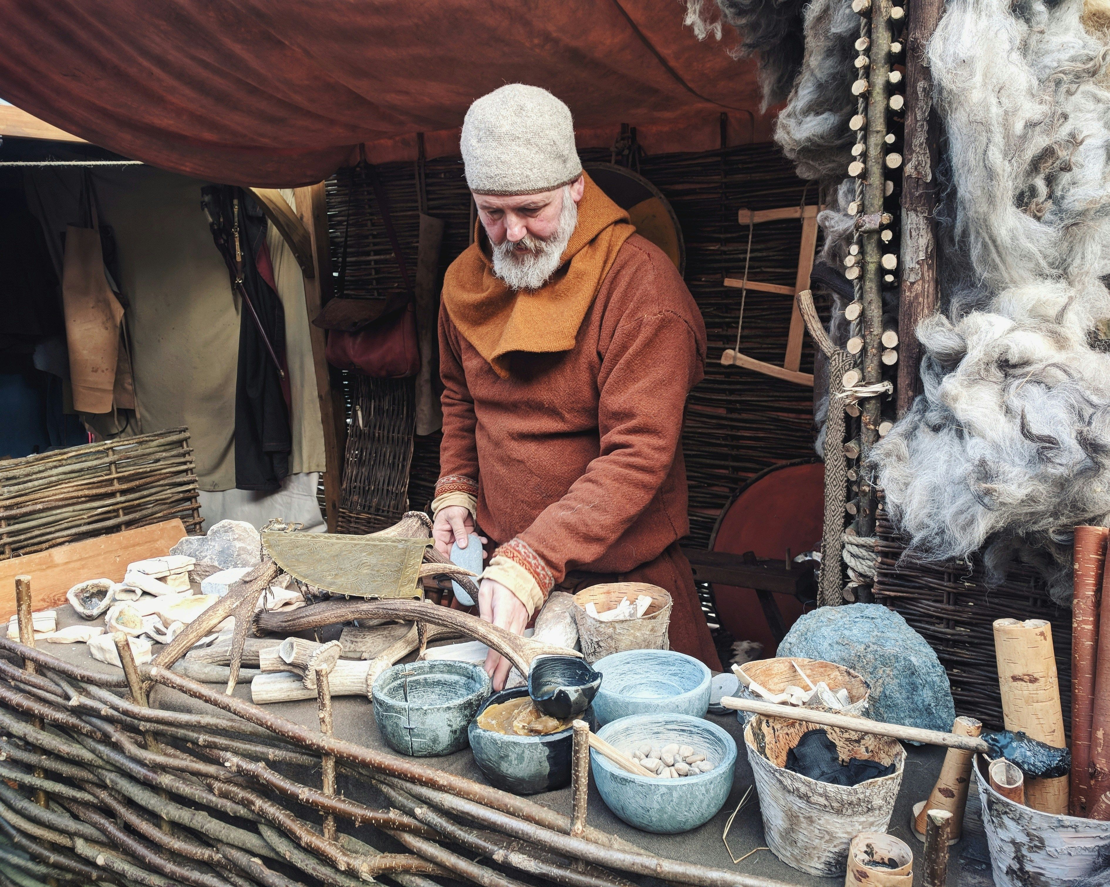 Ein Mann in mittelalterlicher Kleidung steht an einem Stand und verkauft Tonwaren. Vermutlich stammt das Foto von einem Mittelaltermarkt.