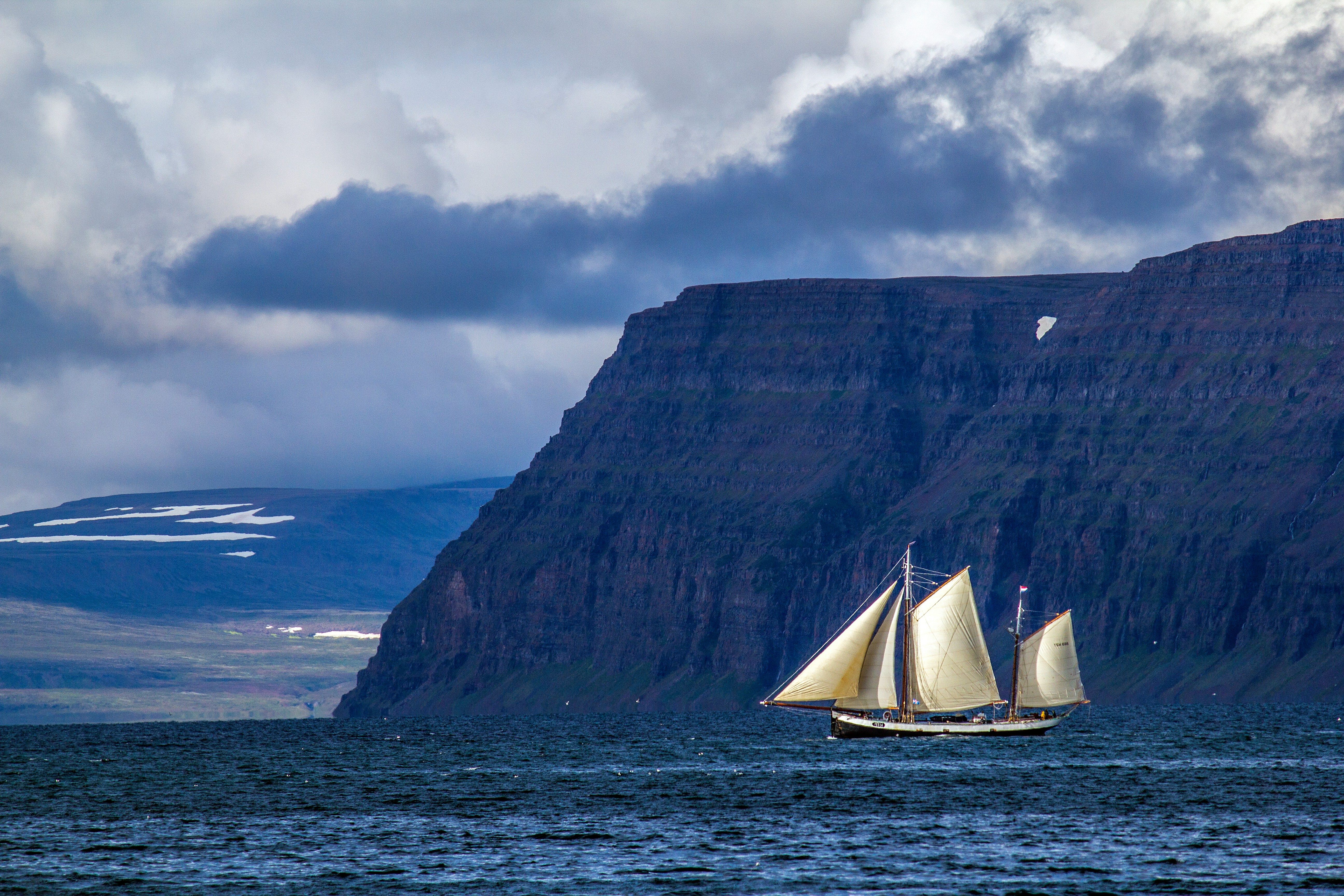 Ein altes Segelschiff fährt vor den majestätischen Westfjorden Islands. Die Stimmung ist märchenhaft, das blaue Meer ruhig.