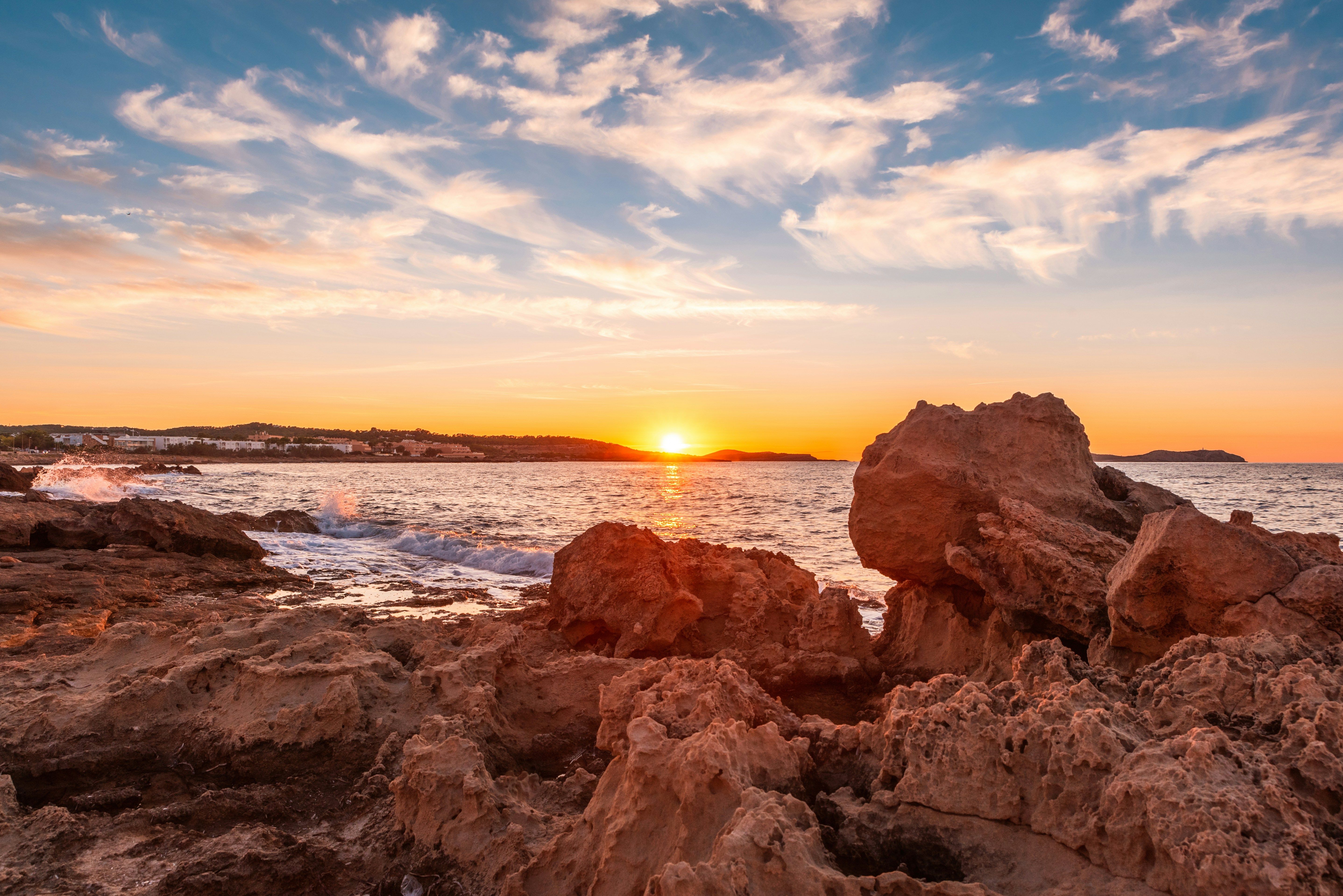 Die Sonne geht über den rauen Felsen und den Wellen Ibizas unter.