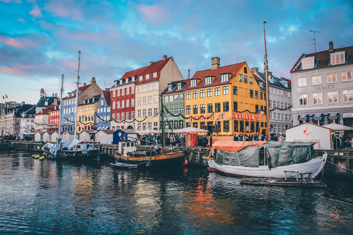 Nyhavn in Kopenhagen. Kleurrijke huizen in typisch Scandinavische stijl liggen aan het water, waar kleine vissersbootjes op het oppervlak drijven.
