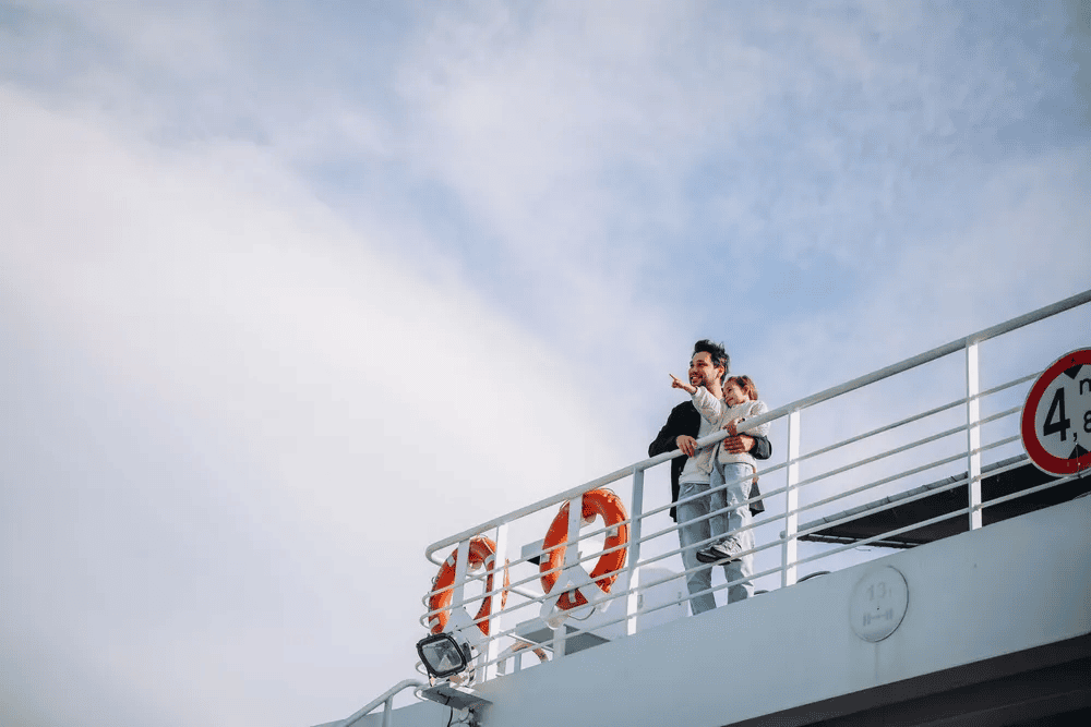 Un hombre y una niña observan el horizonte desde la barandilla de un ferry bajo un cielo despejado.