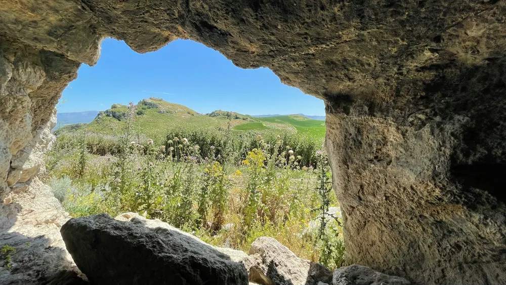 Vista de los campos verdes de Sicilia en primavera desde el interior de una cueva de piedra.