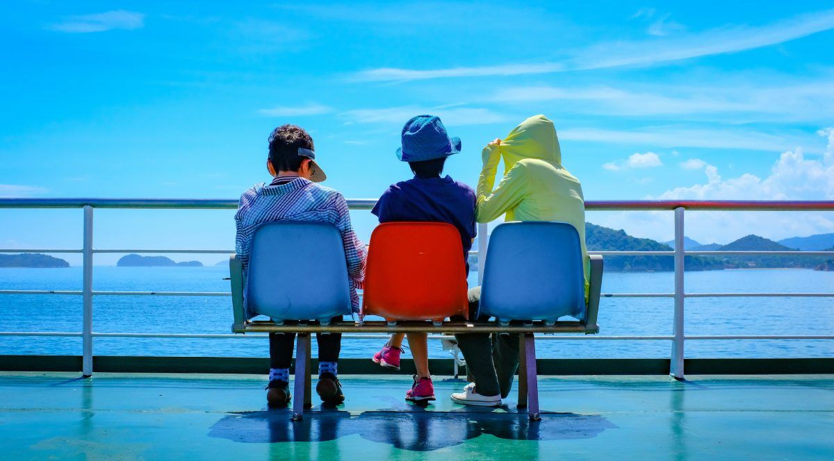 Tres pasajeros sentados en la cubierta de un ferry disfrutando del paisaje marítimo.