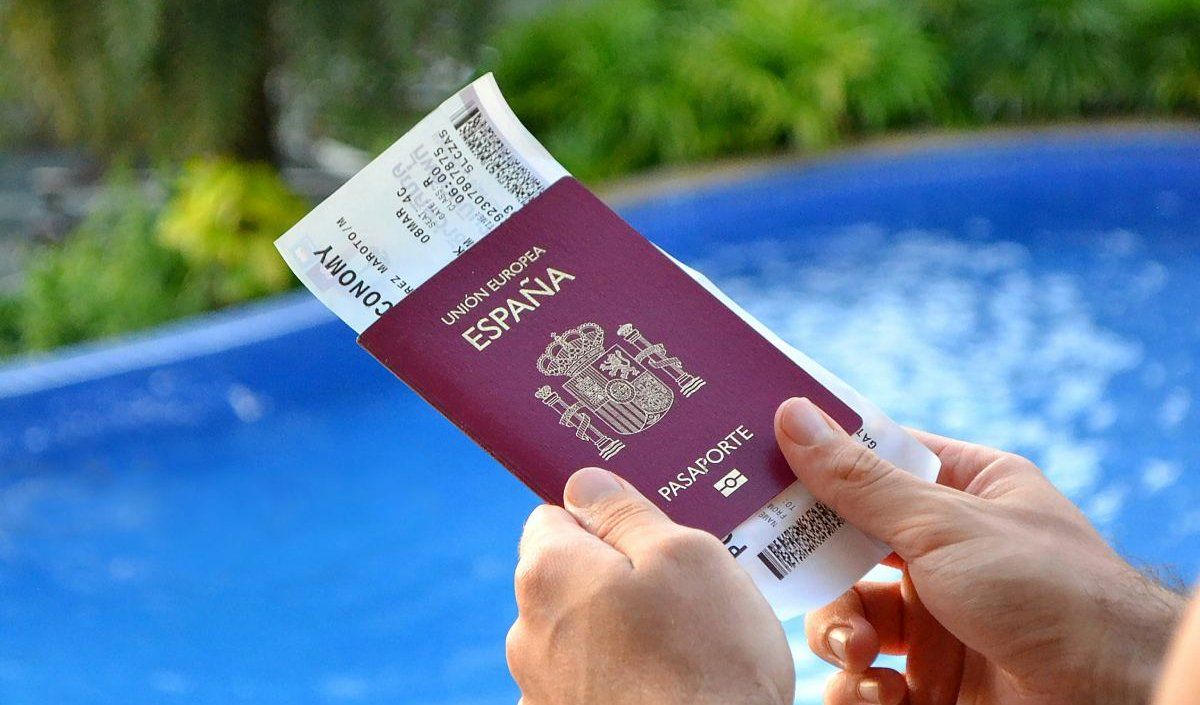 turista sosteniendo un pasaporte español durante sus vacaciones con una piscina de fondo