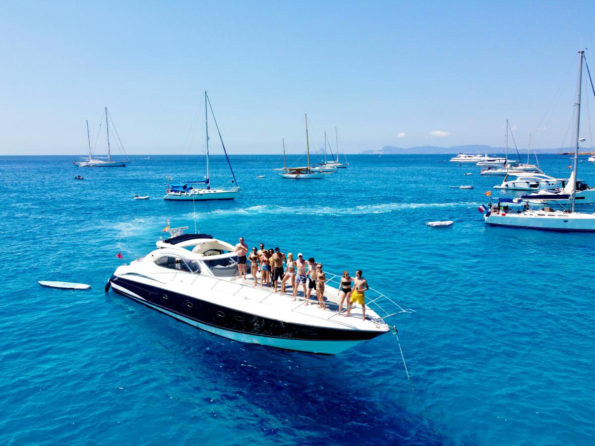 Grupo de amigos disfrutando en un barco frente a la costa de Ibiza en el Mediterráneo