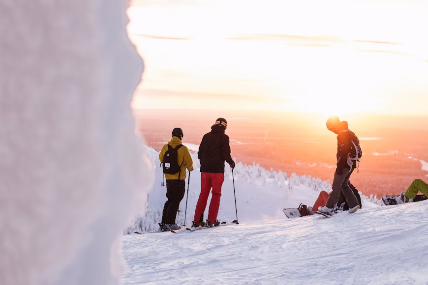 In einer Schneelandschaft in Lappland sieht man drei Menschen. Zwei sind auf Skiern und halten Skistöcke, eine Person geht auf die anderen zwei zu.